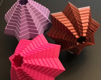 May include: Three 3D printed star-shaped objects. One is a light purple, one is a bright pink, and one is a dark brown.
