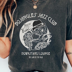 Könnte beinhalten: Dunkelgraues T-Shirt mit einer weißen Grafik eines Skeletts mit Hut und Mikrofon, mit dem Text "BOJANGLES' JAZZ CLUB" und "DOWNSTAIRS LOUNGE". Das Shirt besteht aus einem weichen, bequemen Material.