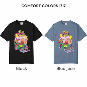 May include: Two short-sleeve t-shirts, one black and one blue jean, featuring the text COMFORT COLORS 1717 at the top. The graphic displays the Jem and the Holograms logo, the year 1985, and the text Truly Outrageous World Tour with colorful band members.