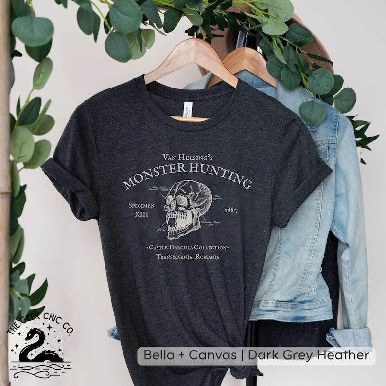 May include: Dark grey heather t-shirt with the text "Van Helsing's Monster Hunting" and a detailed skull graphic. The shirt also includes the text "Specimen XIII" and "1887". The bottom of the shirt reads "Castle Dracula Collection, Transylvania, Romania".