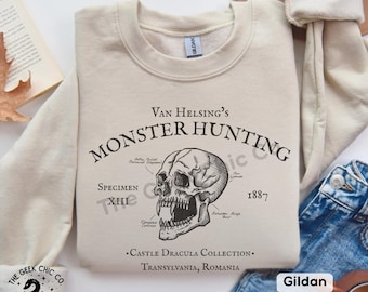 May include: Sand-colored sweatshirt with a graphic that reads "Van Helsing's Monster Hunting" and a detailed skull illustration. The text includes "Specimen XIII" and "1887". The sweatshirt is part of the "Castle Dracula Collection" from Transylvania, Romania.