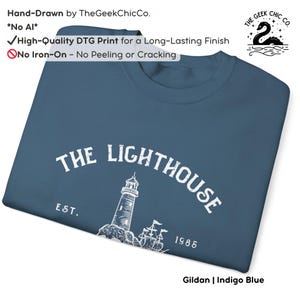 May include: Indigo blue sweatshirt with a white graphic of a lighthouse and the text "THE LIGHTHOUSE EST. 1985". The sweatshirt is hand-drawn by TheGeekChicCo. and features a high-quality DTG print. The sweatshirt is made of Gildan material.