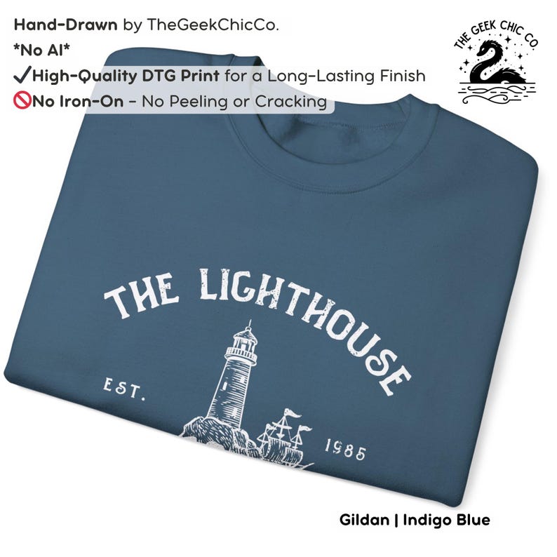 May include: Indigo blue sweatshirt with a white graphic of a lighthouse and the text "THE LIGHTHOUSE EST. 1985". The sweatshirt is hand-drawn by TheGeekChicCo. and features a high-quality DTG print. The sweatshirt is made of Gildan material.