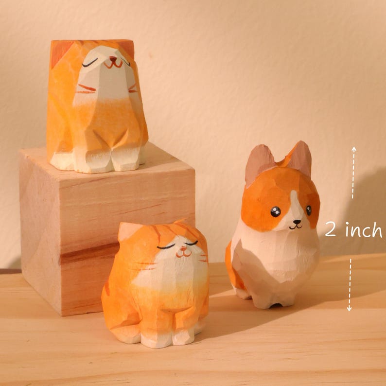 May include: Three wooden cat figurines, one on a wooden block, and a corgi figurine. The cat figurines are orange and white, and the corgi is orange and white. The corgi is approximately 2 inches tall.