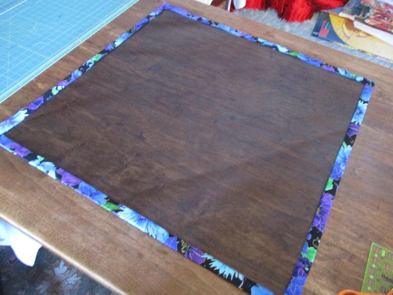 May include: A dark brown wooden board with a floral patterned border in shades of blue, purple, and green. The board is rectangular and appears to be sitting on a wooden surface.
