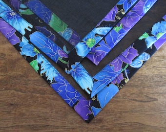 May include: Close-up of several fabric corners with a floral pattern. The fabric features blue and purple flowers with gold accents on a black background. The corners are arranged in a V-shape on a wooden surface.