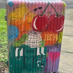 May include: A brightly painted suitcase featuring graffiti art. The design includes cherries, a globe, and the word "IBIZA". The suitcase has a teal and green Tiffany & Co. storefront design, and a rainbow colour scheme.