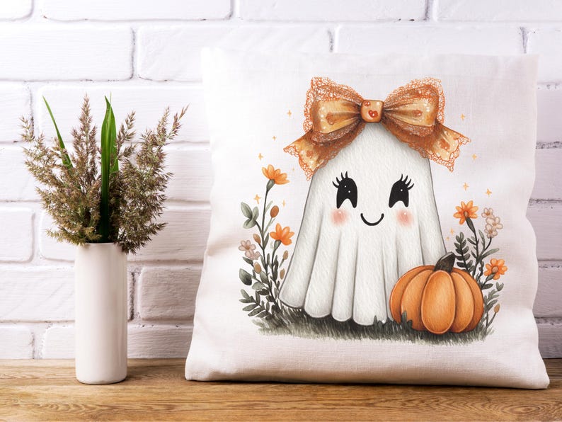 May include: White tote bag featuring a cute ghost illustration with a bow, blush cheeks, and a smiling face. An orange pumpkin and flowers are at the bottom. A vase with decorative grass is on the left.