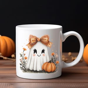 May include: White ceramic mug featuring a cute ghost illustration with a bow and a pumpkin. The ghost has a smiling face and is surrounded by flowers and another small pumpkin. The mug is a Halloween-themed product.