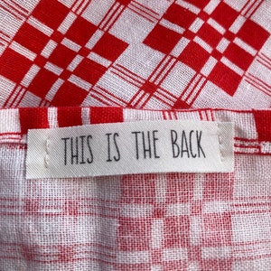 May include: Red and white checkered fabric with a white tag that says "THIS IS THE BACK" in black text.