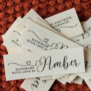 May include: A stack of white fabric labels with black text. The labels read "Handmade with love by Amber".