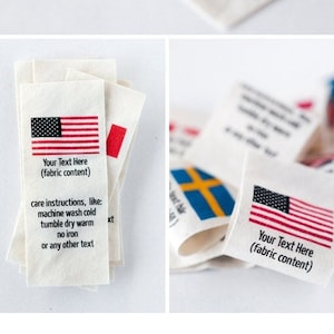 May include: A stack of white fabric labels with different country flags printed on them. The labels include the text "Your Text Here (fabric content)" and care instructions: machine wash cold, tumble dry warm, no iron, or any other text.