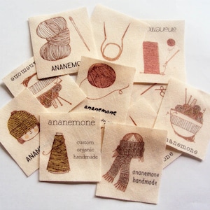 Puede incluir: Una colecci&oacute;n de etiquetas de tela hechas a mano con la palabra "an&eacute;mona" e ilustraciones de hilo, agujas de tejer y una persona con una bufanda. Las etiquetas son de color beige con tinta marr&oacute;n.