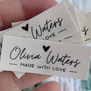 May include: Off-white fabric labels with black script. The labels read "Waters LOVE" and "Olivia Waters MADE WITH LOVE" with a heart symbol. The labels are likely for handmade items.