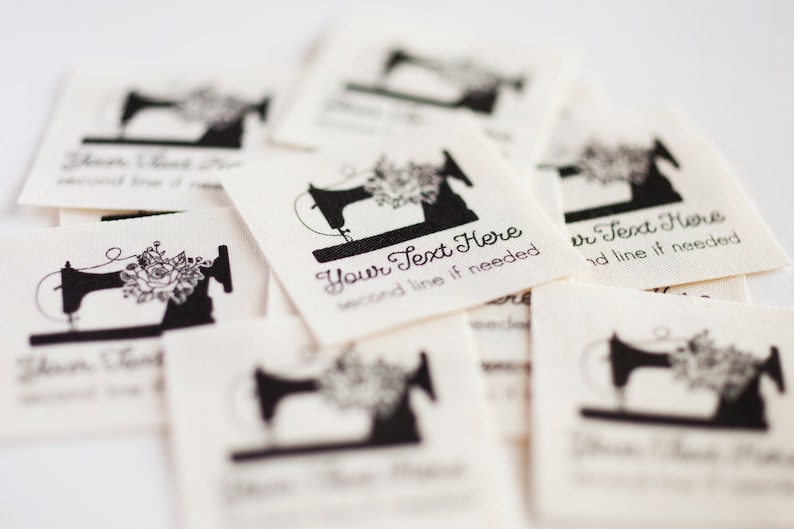 Peut inclure: Une pile d'&eacute;tiquettes en tissu blanc avec un motif de machine &agrave; coudre noire et le texte "Your Text Here second line if needed".