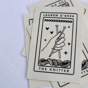 Pode incluir: Um remendo de tecido branco com texto preto e um gr&aacute;fico de uma m&atilde;o segurando agulhas de tric&ocirc;. O texto diz "Lauren O'Shea The Knitter".