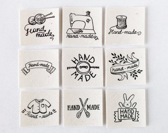 May include: Nine different hand-drawn designs for handmade labels. The designs include a sewing machine, yarn and needles, a spool of thread, a banner with the words "Hand-made", a button with the words "HAND MADE", a banner with the words "hand-made" and leaves, a shirt with the words "Hand-made", scissors with the words "HAND MADE", and a bunny holding a banner with the words "HAND MADE".