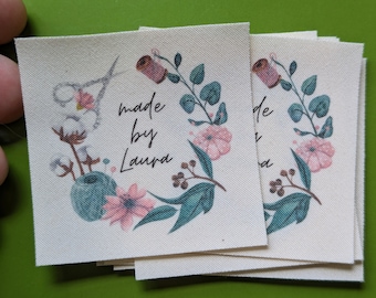May include: A stack of white fabric labels with a floral design and the text "made by Laura".