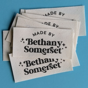 Puede incluir: Una pila de etiquetas de tela blanca con texto negro que dice "Made by Bethany Somerset".