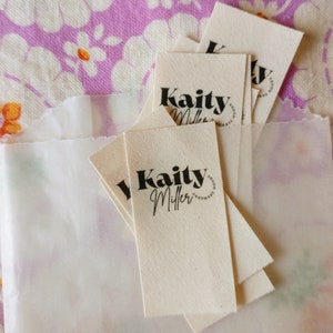 May include: A stack of white fabric tags with black text that reads "Kaity Miller Goods Handmade".