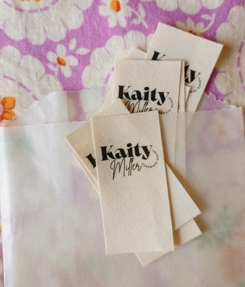 May include: A stack of white fabric tags with black text that reads "Kaity Miller Goods Handmade".