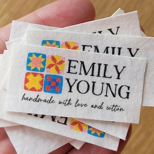 May include: A stack of white fabric labels with a colorful patchwork design and the text "EMILY YOUNG handmade with love and cotton".