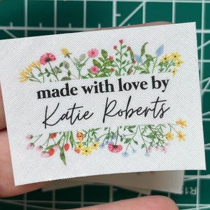 May include: White fabric label with a floral border and the text "made with love by Katie Roberts".