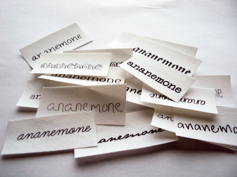 May include: A pile of white paper scraps with the word "anemone" written on each one in black ink. The word is spelled differently on each scrap, with some variations in the lettering.