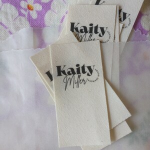 May include: A stack of white fabric tags with black text that reads "Kaity Miller Handmade Goods".