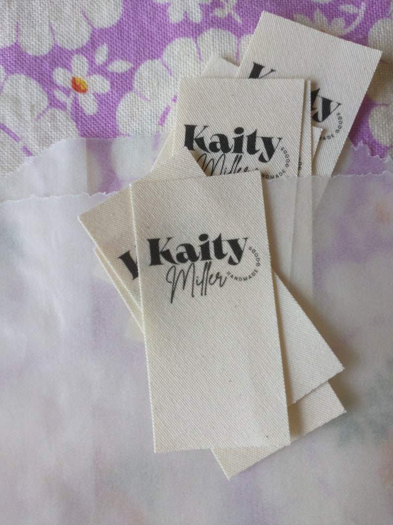 May include: A stack of white fabric tags with black text that reads "Kaity Miller Handmade Goods".