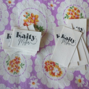 May include: A stack of white fabric labels with black text that reads "Kaity Miller Handmade Goods".