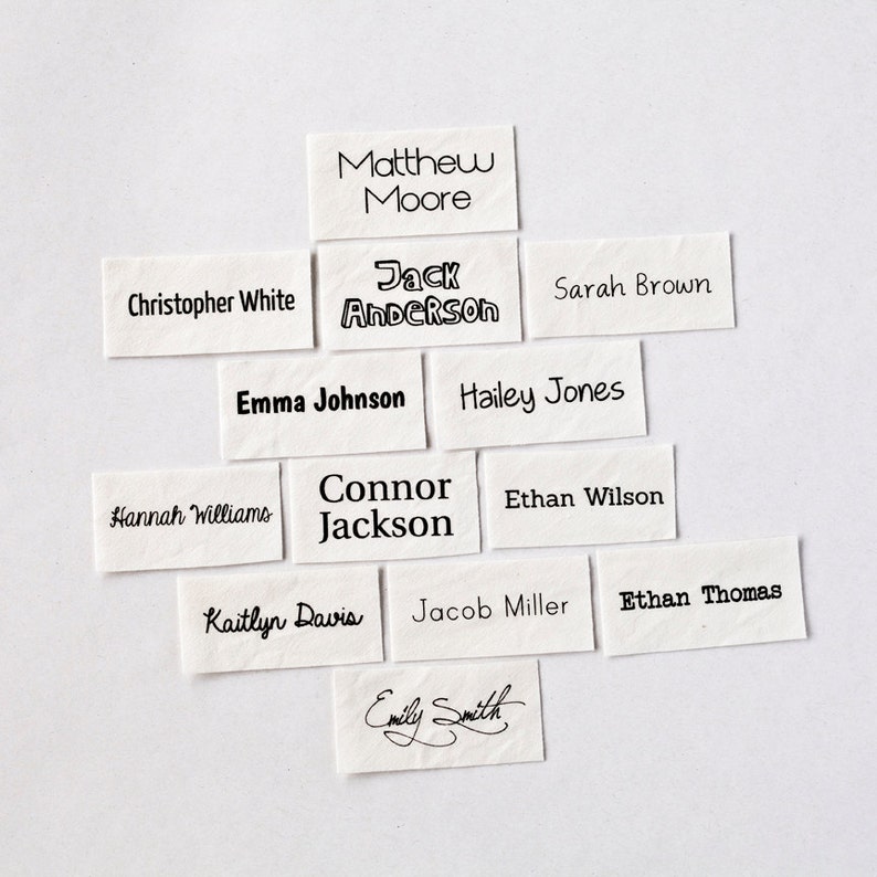 May include: A collection of white paper tags with black ink, each featuring a different name. The names include Matthew Moore, Jack Anderson, Sarah Brown, Christopher White, Emma Johnson, Hailey Jones, Hannah Williams, Connor Jackson, Ethan Wilson, Kaitlyn Davis, Jacob Miller, Ethan Thomas, and Emily Smith.