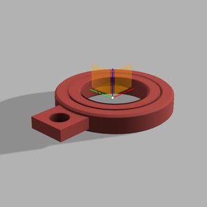 Puede incluir: Objeto renderizado en 3D, de color marrón rojizo, con un diseño circular y una extensión rectangular. Presenta un agujero central y otro más pequeño en la extensión, sugiriendo una pieza mecánica.