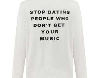 Può includere: Maglietta bianca a maniche lunghe con la scritta nera: "STOP DATING PEOPLE WHO DON'T GET YOUR MUSIC". La maglietta ha un girocollo e una vestibilità ampia, adatta per un look casual.