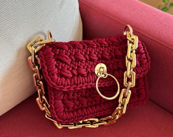 May include: A small, red crocheted handbag with a gold chain strap and a gold ring accent.