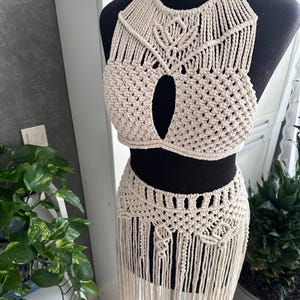 May include: A white crocheted halter top and skirt set with fringe detailing. The top has a keyhole opening in the front and the skirt has a geometric pattern.