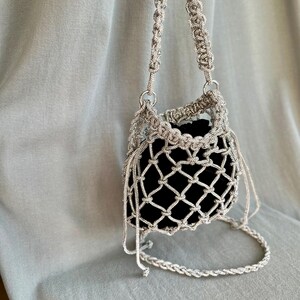 Può includere: Una borsa a catena argentata con fodera in velluto nero. La borsa è realizzata con un design a rete e ha una tracolla lunga.