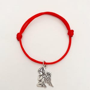 Op de afbeelding: Rode koordarmband met een zilverkleurige engelbedel. De bedel toont een knielende engel met gedetailleerde vleugels. De armband is verstelbaar met schuifknopen.