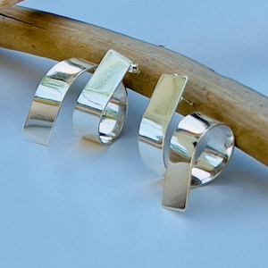 May include: A pair of silver earrings with a unique, swirling design. Each earring features a rectangular post that curves into a spiral shape. The earrings are highly polished and reflect light, creating a bright, shiny appearance.