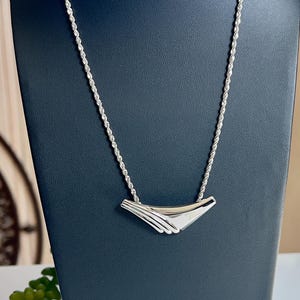 May include: A silver necklace with a rope chain and a curved pendant. The pendant has a geometric design with multiple layers.