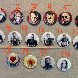 以下が含まれることがあります： ホラー映画のキャラクターが描かれた丸いボタンのセットです。ボタンは1から16まで番号が付けられており、フレディ・クルーガー、ジェイソン・ボーヒーズ、マイケル・マイヤーズなどのキャラクターが描かれています。