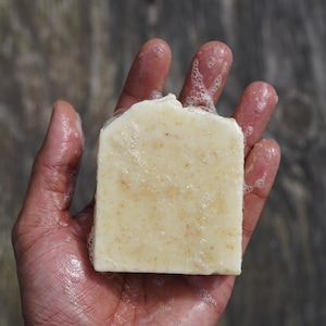 Könnte beinhalten: Eine weiße Seife mit körniger Textur, die in einer Hand mit Seifenblasen gehalten wird.