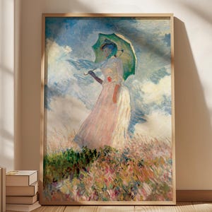 May include: A framed print of a woman holding a green parasol in a field of flowers. The artwork features a woman in a long white and pink dress, with a blue scarf, standing in a field of colorful flowers. The background is a cloudy sky.