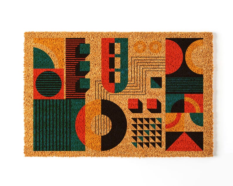 May include: A rectangular doormat with a geometric design. The design features shapes in teal, orange, red, and black. The doormat is made of a natural fiber material.