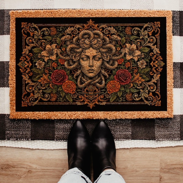 May include: A rectangular doormat with a natural tan fiber border and a black center panel. The center features a detailed illustration of a stone-like face with snakes for hair, surrounded by intricate floral patterns including red roses.