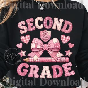 Könnte beinhalten: Ein schwarzes Sweatshirt mit einer rosa Grafik und dem Text SECOND GRADE. Das Design umfasst eine große Schleife, einen Bleistift, Herzen, Sterne und ein Schild mit der Zahl 2, alles verziert mit verschiedenen rosa Karos, Punkten und Zickzackmustern.
