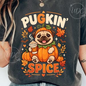 May include: A charcoal gray t-shirt featuring a graphic of a pug wearing a pumpkin costume, holding a coffee cup. The text reads PUGKIN SPICE. The design includes orange pumpkins, red and orange autumn leaves, small bats, and stars.