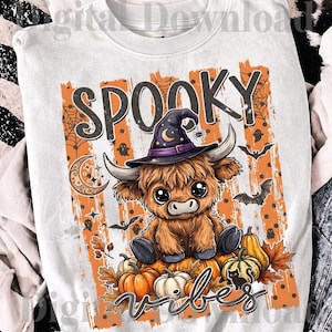 Peut inclure: Un sweat-shirt blanc à col rond avec un motif de vache Highland brune portant un chapeau de sorcière violet. Le design inclut des rayures verticales orange, des citrouilles, des chauves-souris, des fantômes, un croissant de lune et le texte SPOOKY VIBES.
