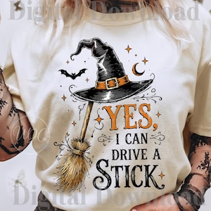 Può includere: Una t-shirt color crema con la grafica di un cappello da strega nero appoggiato su una scopa. Il disegno include un piccolo pipistrello, una luna crescente e stelle. Il testo recita YES, I CAN DRIVE A STICK, in caratteri arancioni e neri.