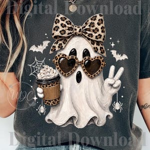 Peut inclure: Un t-shirt gris foncé avec un motif de fantôme blanc portant des lunettes de soleil en forme de cœur à imprimé léopard et un nœud assorti. Le fantôme tient un gobelet à café léopard avec de la crème fouettée et fait un signe de paix, entouré de chauves-souris.